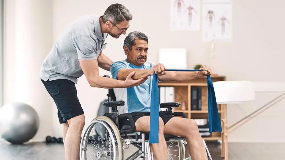physio therapist assisting a man in a wheelchair in an exercise