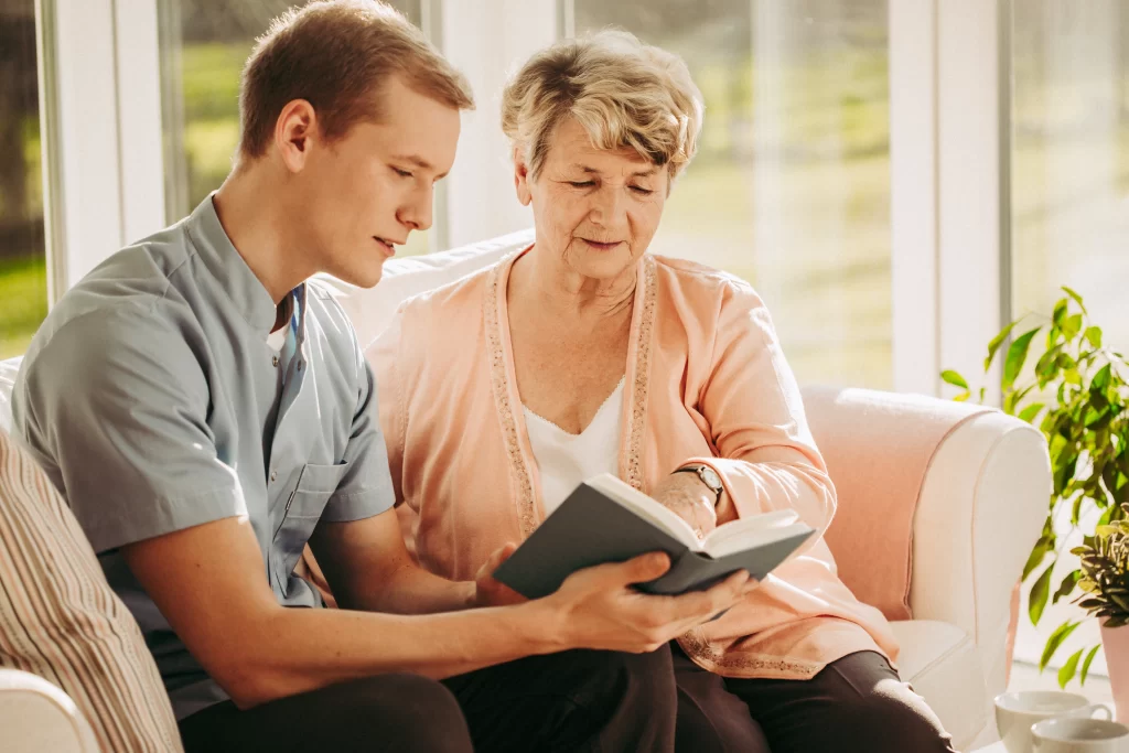 caregiver reading from a book to an elderly lady