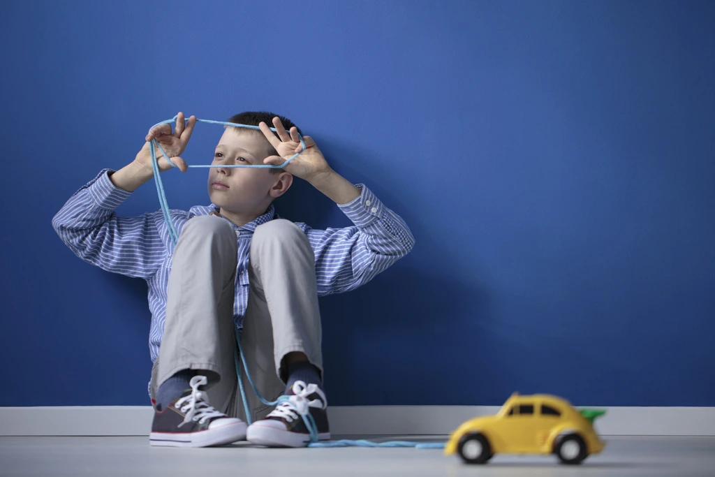 a boy with aspergers sitting with his back against the wall and playing with a tape