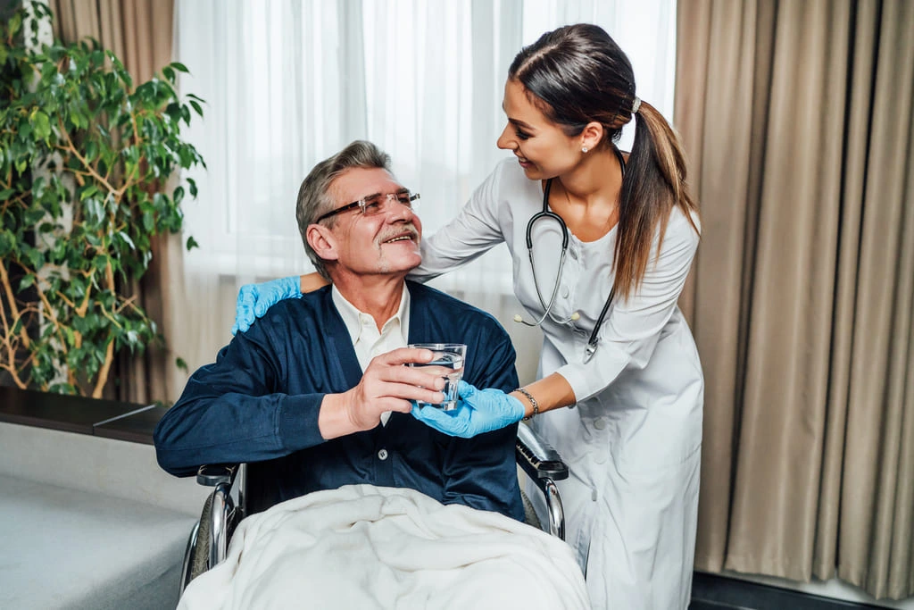 older man-wheelchair-smiles-nurse assistant she hands him glass water