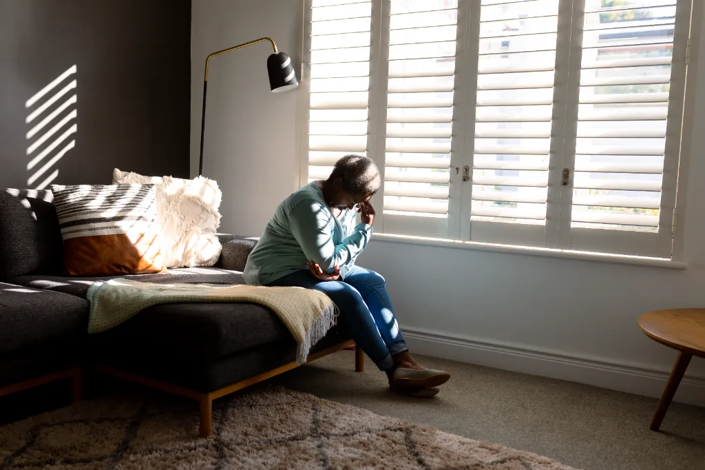 elderly african american lady sitting on the edge of her bed and thinking