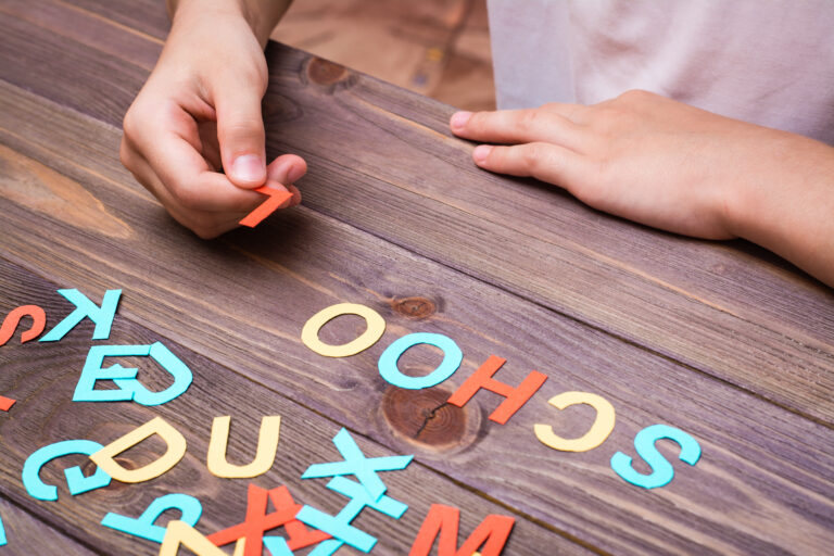 a child trying to speel the word school with letters