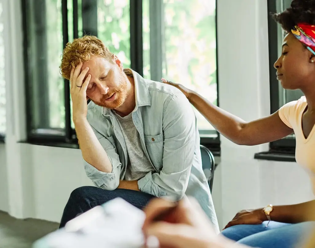 man holding his head being comforted by support worker