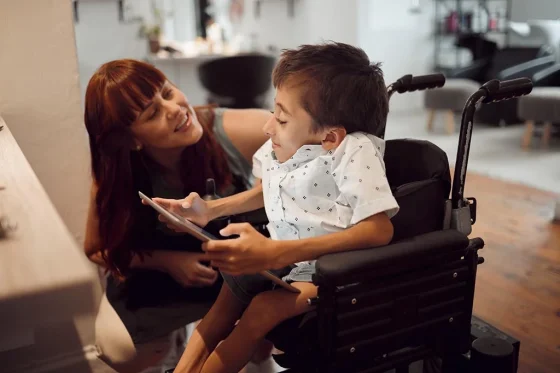 a young boy with complex needs holding a tablet with his caregiver