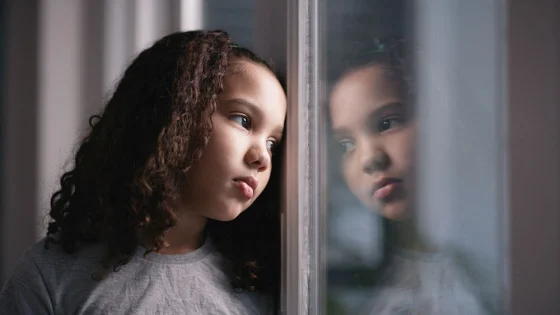 autistic little girl looking through window glass