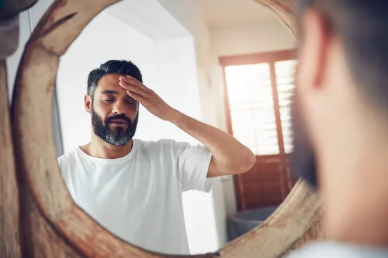 man looking at self in the mirror and holding his forehead